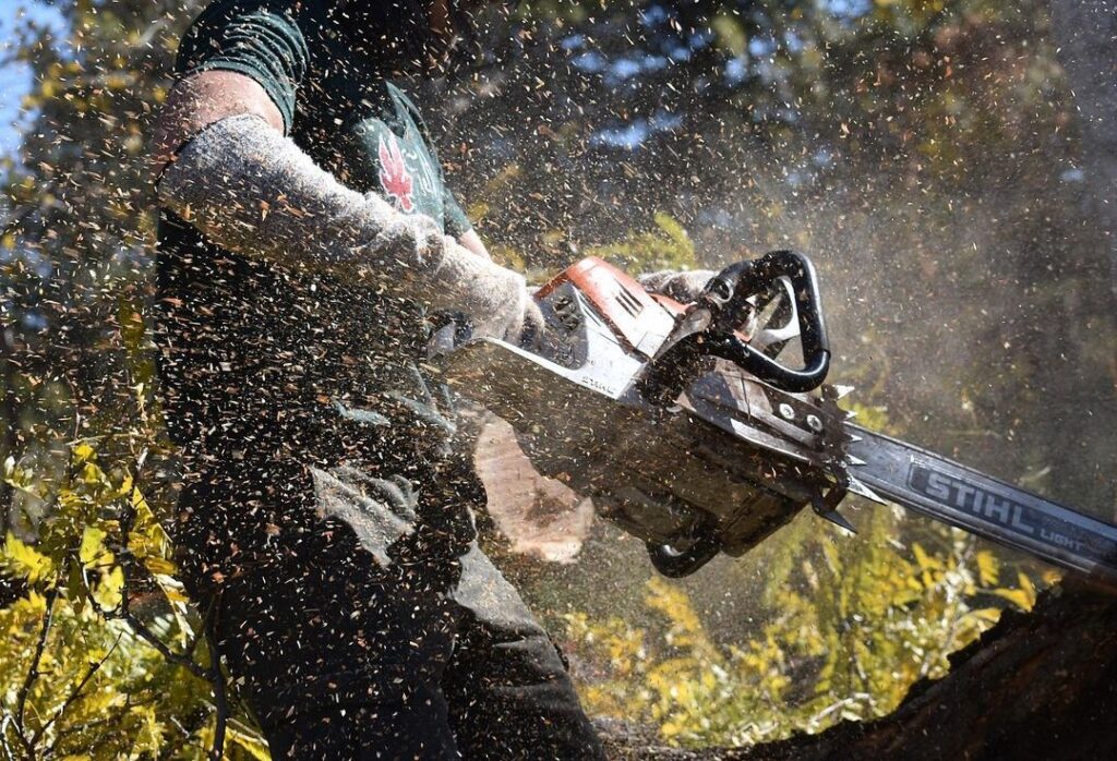 A closeup shot of a man's arms holding a chainsaw. 
