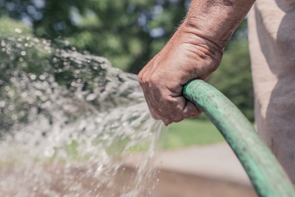 A close up of a someone's hand, outdoors, holding a hose that is squirting water out of it.